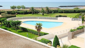 Una piscina de borde curvo, rodeada de vegetación cuidada y vista al mar.