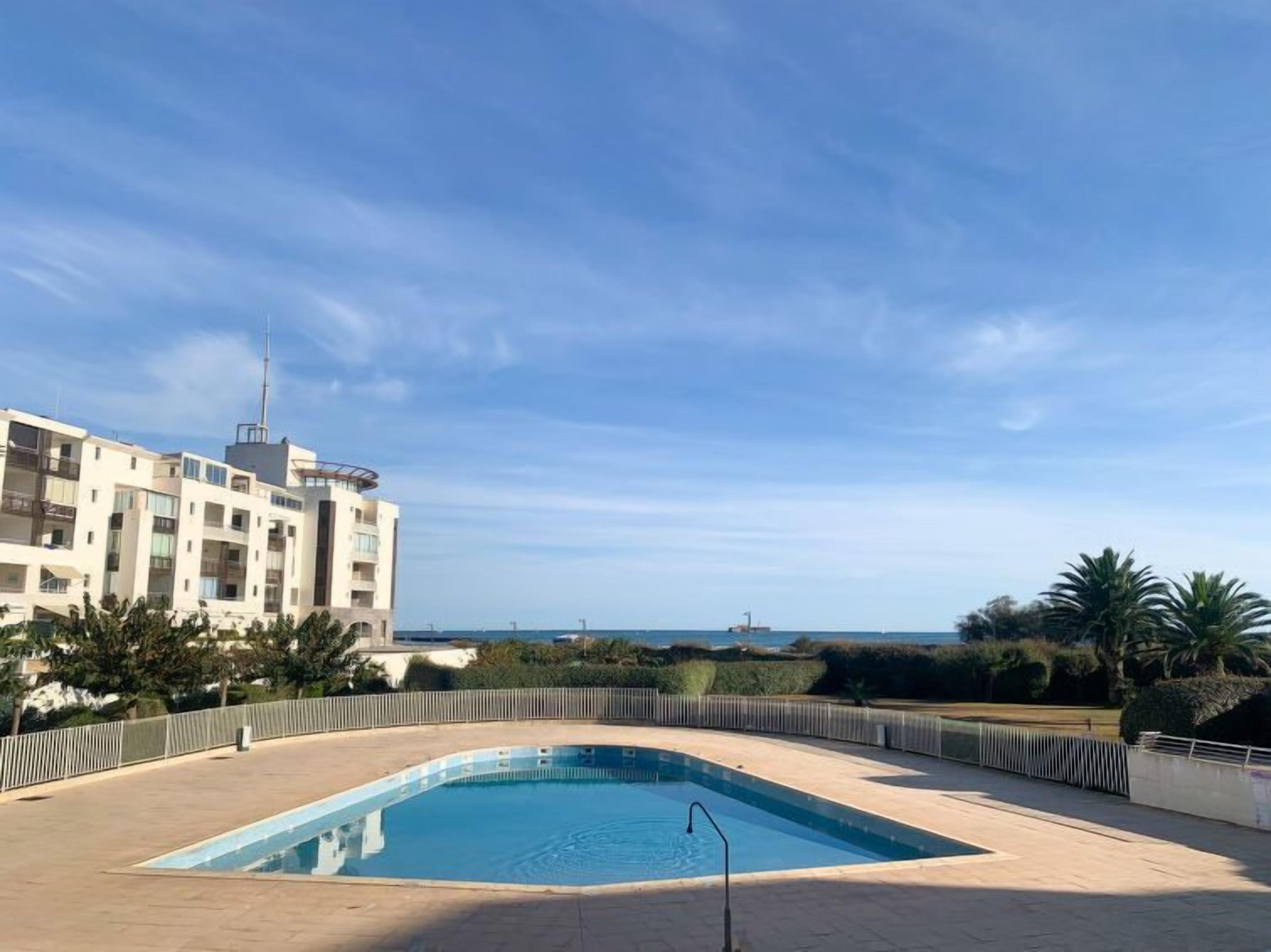 Una piscina con vistas al mar, rodeada de una valla y palmeras.