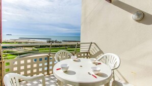 Un balcón con una mesa y sillas blancas, con vista a una playa y al océano.