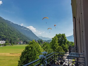 Een balkon met uitzicht op een bergachtig landschap, een groen veld en een heldere lucht.