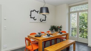 A dining area with a wooden table, orange chairs, a bench, a hanging light, and a view through a large window. - Apartment Modern by Interhome (Interlaken)
