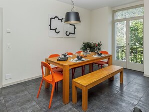 Een eetruimte met een houten tafel, oranje stoelen, een bank, een hanglamp en uitzicht door een groot raam.