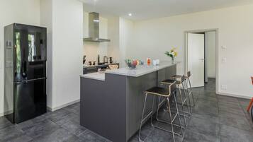 Eine moderne Küche mit einer zentralen Kochinsel, Barhocker, einem Kühlschrank und einer sichtbaren Tür zu einem anderen Raum.