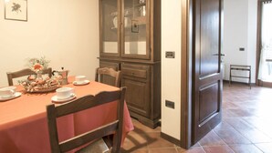 A dining area with a table set for two, a cabinet with glass doors, and a door leading to another room. - Montecorneo by Interhome (Perugia)