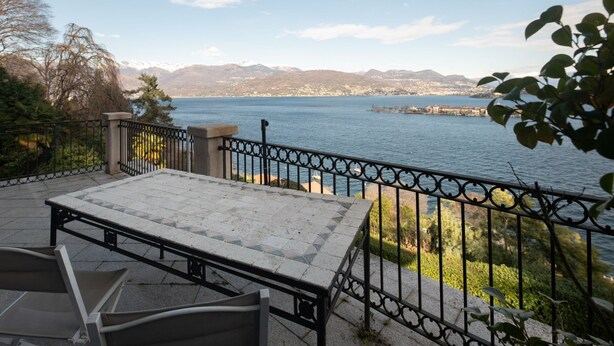 Um terraço com mesa e cadeiras com vista para um lago, e montanhas ao fundo.