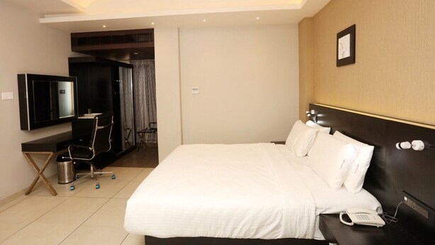 A modern hotel room with a large bed, a desk with a chair, a TV, and a telephone. - lnbresidency (Tirupati)