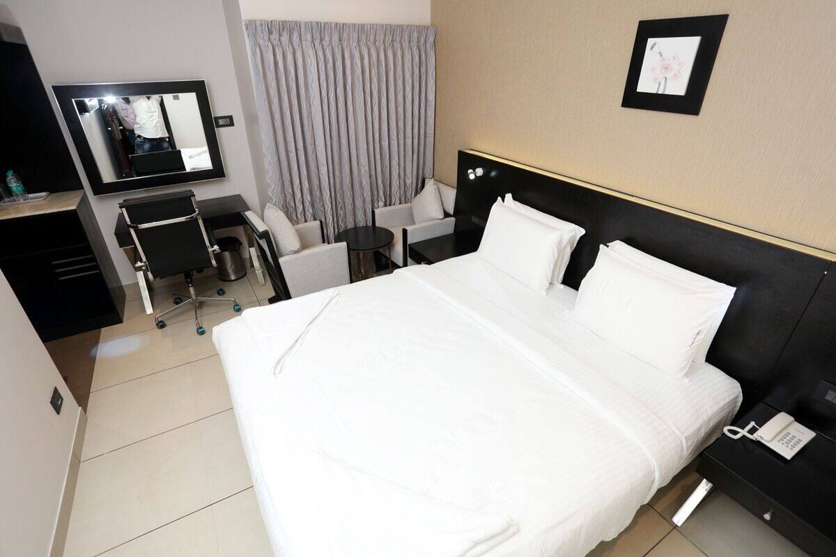 A hotel room with a large bed, a desk with a chair, a small table, a mirror, and a telephone.