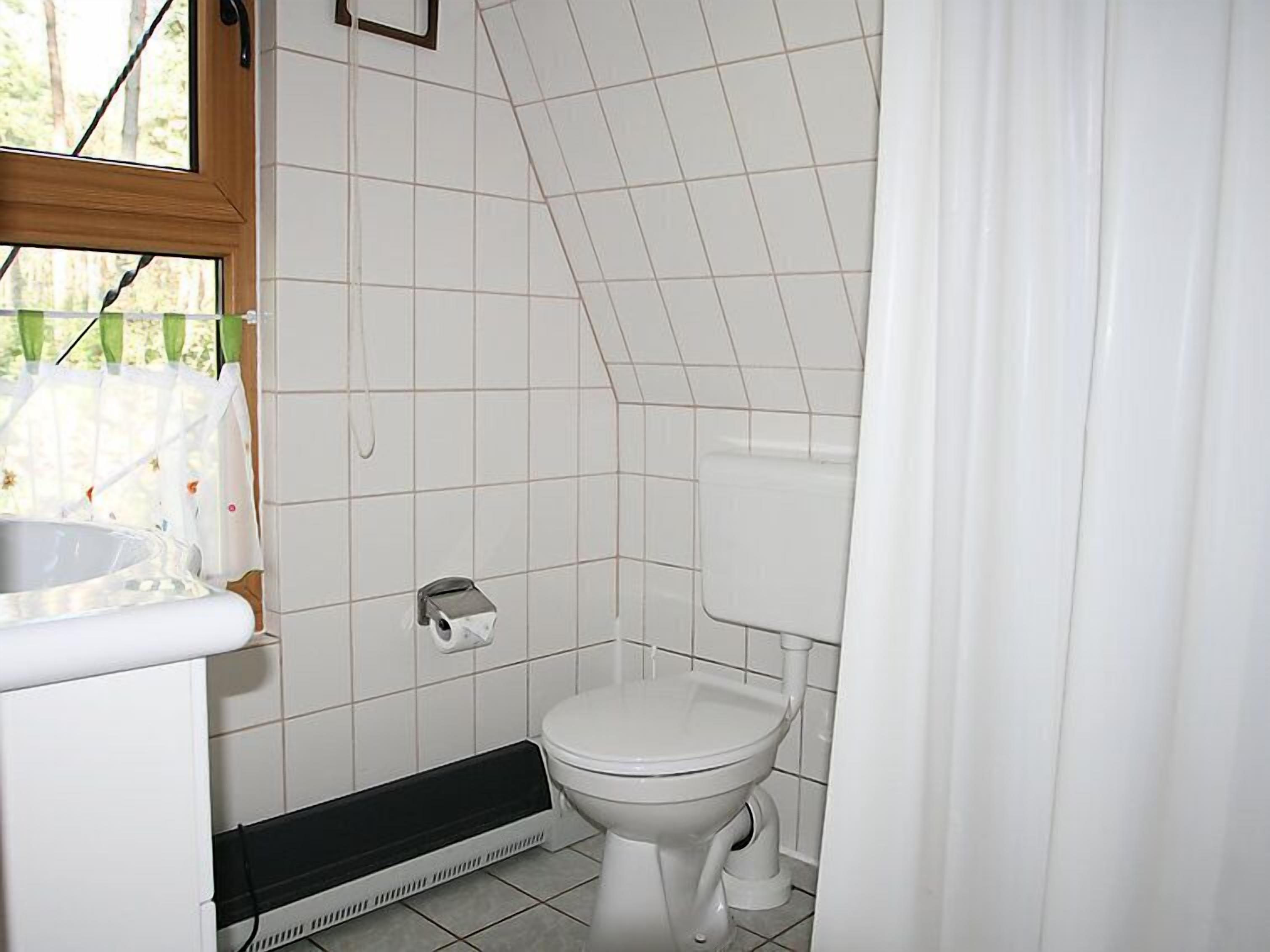 Une petite salle de bain propre, équipée de toilettes, d’un lavabo blanc et d’un radiateur.