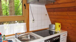 Pieni, käytännöllinen keittiö, jossa on pesuallas, liesi ja ikkuna, josta avautuu näkymä vehreään maisemaan.