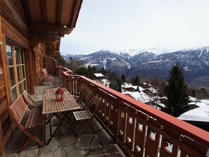 Un balcón de madera con una mesa y sillas, con vistas a un paisaje montañoso con picos nevados.