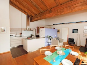 A modern kitchen with white cabinets, a wooden ceiling, and a dining area with a wooden table set for four.