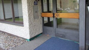 A building entrance with a textured wall, a door with a wooden handle, and a blue mat at the entrance. - Apartment Walter by Interhome (Bad Hofgastein)