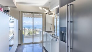 Una cocina moderna con un refrigerador grande, un lavamanos y vista al mar a través de un portón corredizo de vidrio.