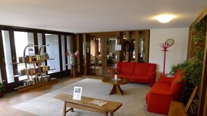 A spacious lobby with a red sofa, a wooden coffee table, and a bookshelf. - Ringstrasse Apt 423 by Interhome (Leukerbad)