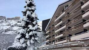A snow-covered building with multiple balconies, a parking sign, and a snow-laden tree. - Ringstrasse Apt 423 by Interhome (Leukerbad)
