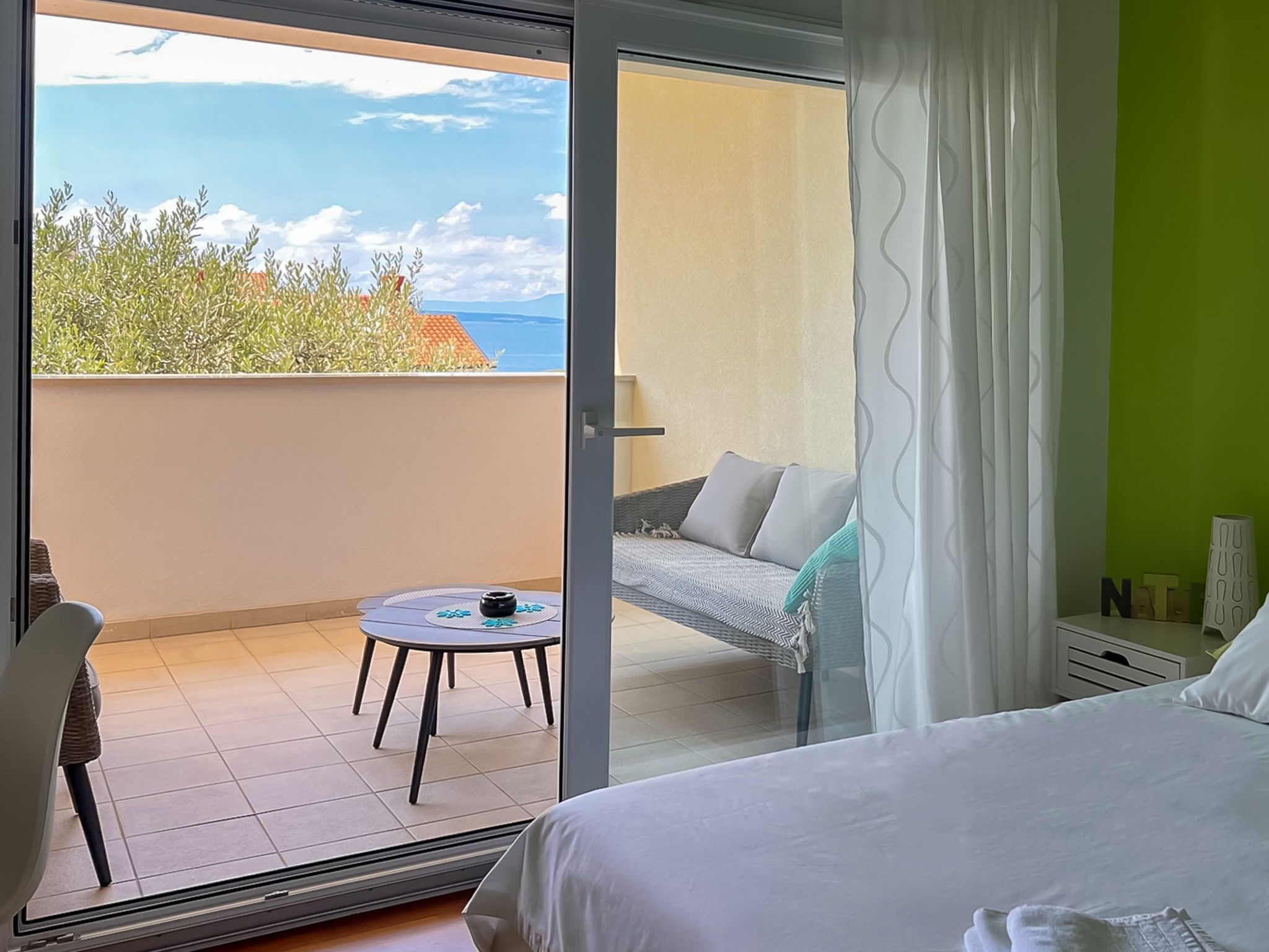 Een hotelkamer met balkon, een bed, een klein tafeltje met een kleedje en een stoel.