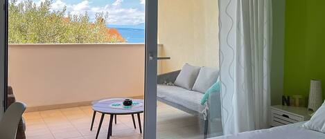 A hotel room with a balcony, a bed, a small table with a mat, and a chair.
