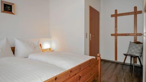 A bedroom with a wooden bed, a nightstand with a lamp, a wooden chair, and a wooden cross on the wall. - Edelweiss by Interhome (Werfenweng)