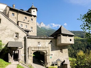 Ein historisches Steinhaus mit steilem Dach, einem Turm und einem großen Rundbogenportal.