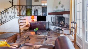 Un salon chaleureux avec une cheminée, des canapés en cuir, une table basse en bois et un escalier menant à un niveau supérieur.