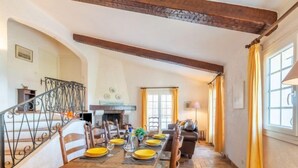 Un coin repas avec une table en bois dressée pour six personnes, entourée de chaises, dans une pièce dont le sol présente un motif en chevrons et où les poutres en bois sont apparentes.