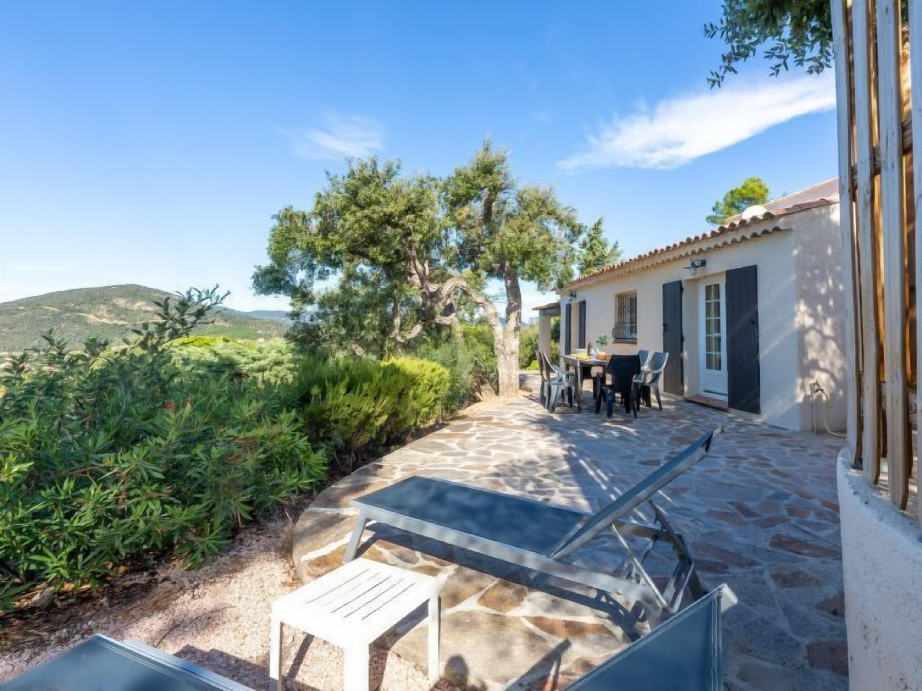 Une terrasse en pierre avec une table et des chaises, une petite table blanche et un grand arbre.