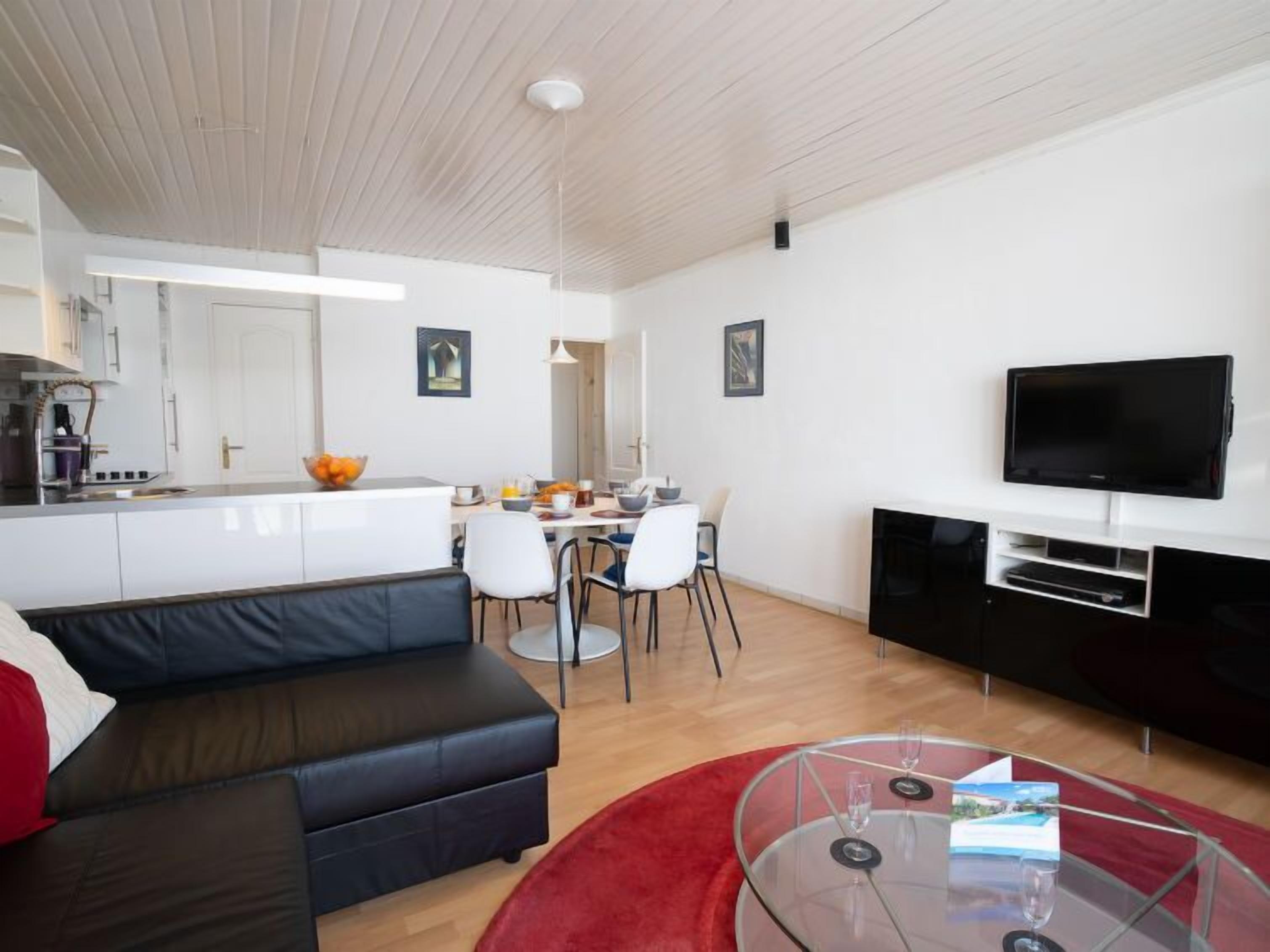 Un salon moderne avec un canapé en cuir noir, une table basse en verre et un tapis rouge.