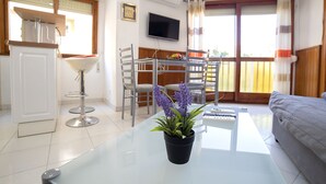 A modern living room with a glass coffee table, a sofa, a dining area with chairs, a TV mounted on the wall, and a balcony with a view. - Playsol by Interhome (Calpe/Calp)