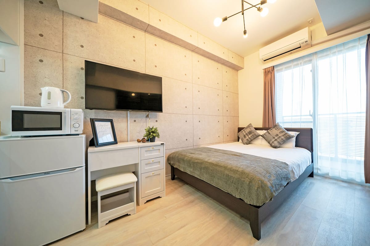 Ein modernes Schlafzimmer mit einem Bett, einem Schreibtisch mit Mikrowelle, einem Fernseher und einer kleinen Sitzecke.