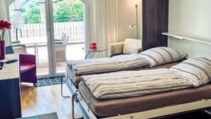A modern bedroom with two beds, a desk, and a chair. There is a balcony with a view of greenery. - Apartment A01 by Interhome (Leukerbad)