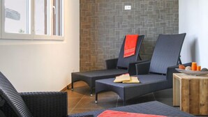 A room with wicker furniture, a tiled floor, and a brick-patterned wall. - Apartment A01 by Interhome (Leukerbad)