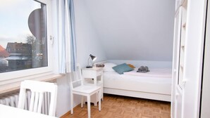 Una habitación pequeña y luminosa con una cama, un escritorio y una silla.