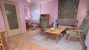 Una sala de estar con piso de madera, un sofá, dos sillones, una mesita de centro y una estantería.