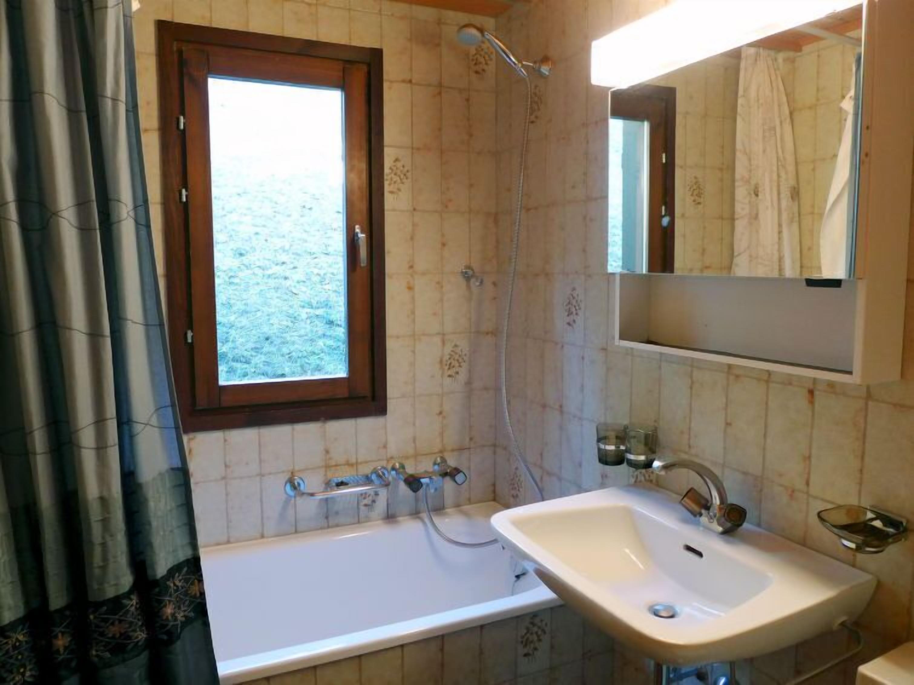 A bathroom with a bathtub, sink, and shower. There is a window above the bathtub and a mirror above the sink.