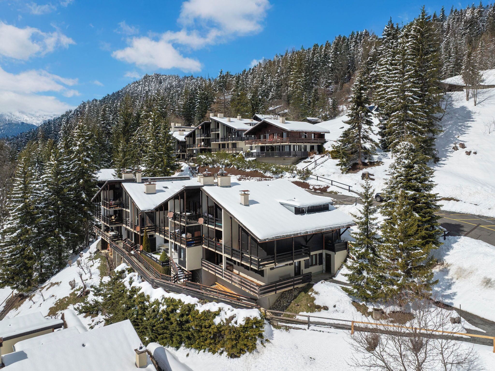 Une station de ski moderne comprenant plusieurs bâtiments, dont un grand chalet doté de balcons et un plus petit chalet.