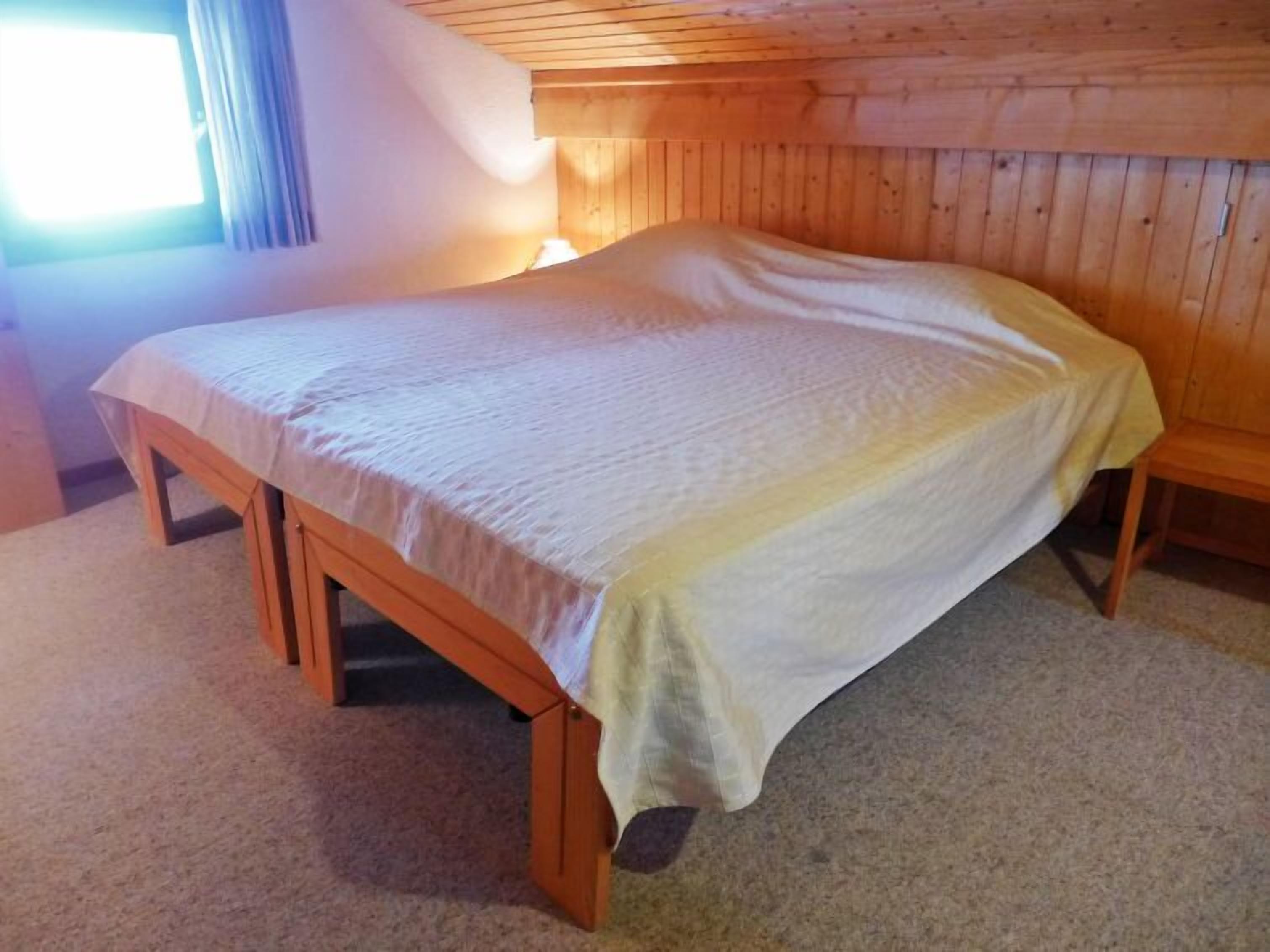 A single bed in a room with wooden walls and a window.
