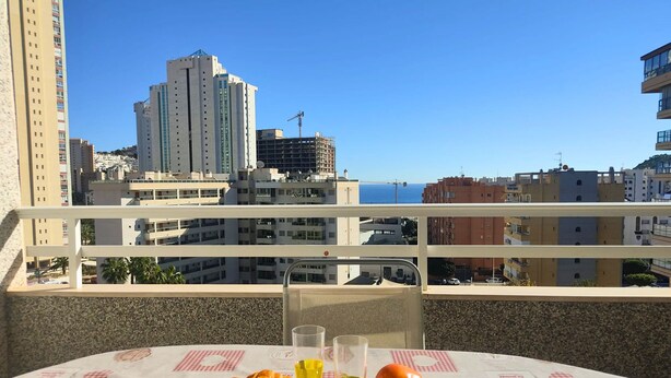 Un balcon avec une table dressée pour le petit-déjeuner, d’où l’on peut admirer un paysage urbain avec ses bâtiments et un ciel dégagé.