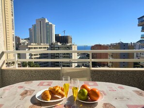 Un balcon avec une table dressée pour le petit-déjeuner, d’où l’on peut admirer un paysage urbain avec ses bâtiments et un ciel dégagé.