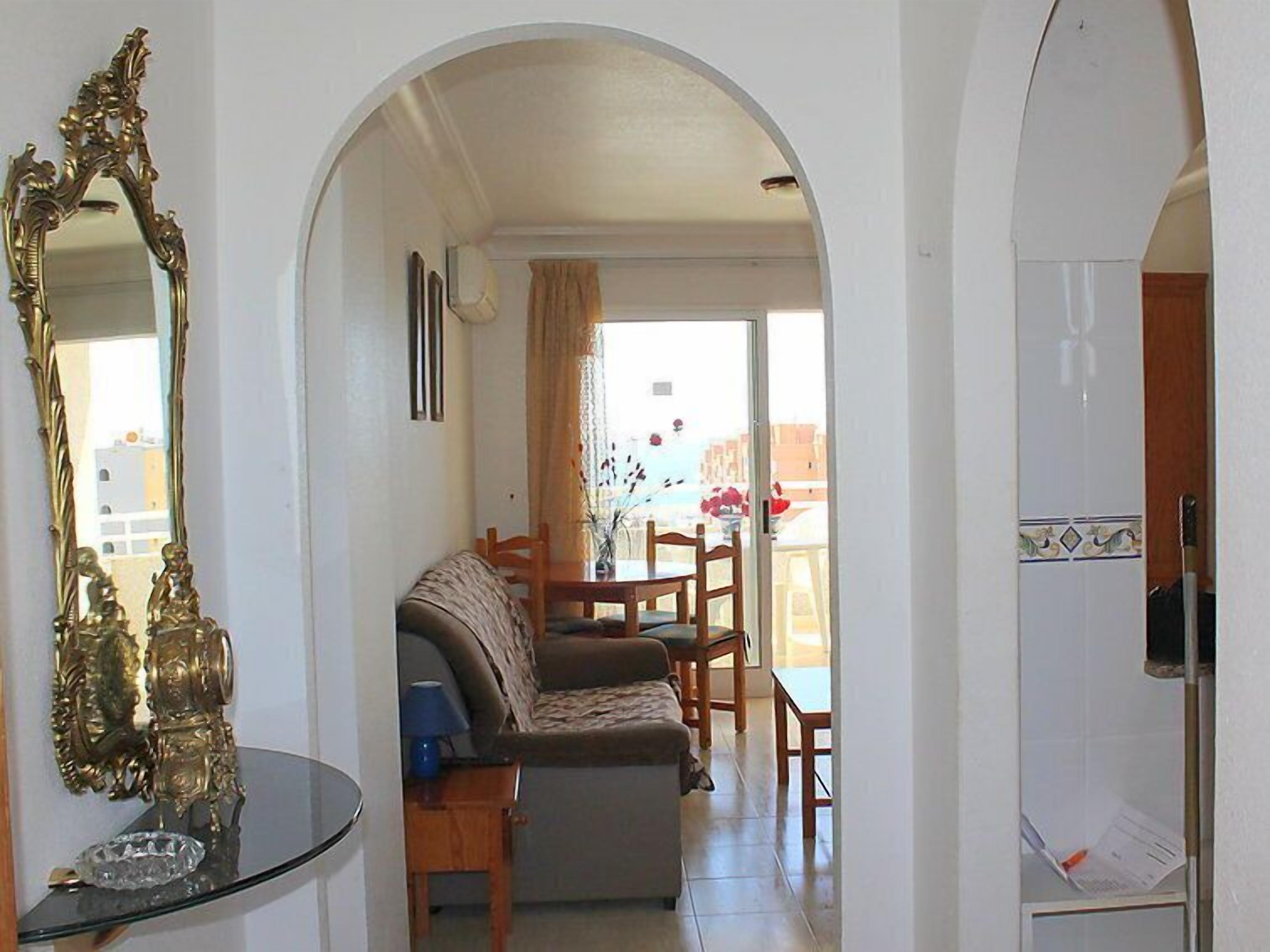 A living room with a sofa, a dining table with chairs, a glass coffee table, and a decorative mirror.