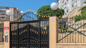 Une entrée fermée par un portail sur lequel est apposée une pancarte interdisant le passage, un mur de pierre et, au fond, un bâtiment doté de balcons.