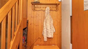 Interior de madera con una escalera de madera, un banco y un perchero con un abrigo blanco.