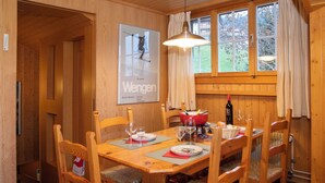 Un comedor de madera con una mesa dispuesta para cuatro, sillas, un cartel en la pared y una ventana con cortinas.