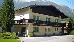 A two-story chalet with a balcony, surrounded by lush greenery and snow-capped mountains in the background. - Kaufmann by Interhome (Pians)