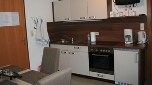 A compact kitchen with a stove, oven, and refrigerator, a small dining area with a table and chair, and a television mounted above the counter. - Kaufmann by Interhome (Pians)