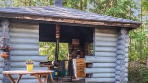 Une cabane rustique en rondins de bois, dotée d’un petit porche, d’une table et de chaises.
