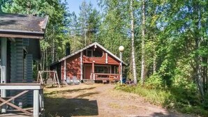 Une cabane avec une véranda, un chemin de terre menant à celle-ci, et une forêt en arrière-plan.