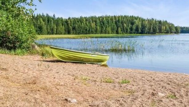 Un bateau sur une plage de sable, au bord d’un lac paisible, avec une forêt dense en arrière-plan.