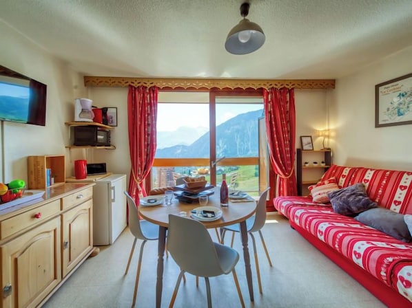 Una sala de estar acogedora con una mesa de comedor, sillas, un sofá rojo y un televisor en la pared.