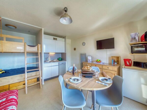 Una habitación compacta con literas, kitchenette, mesa de comedor con sillas y un televisor de pantalla plana.