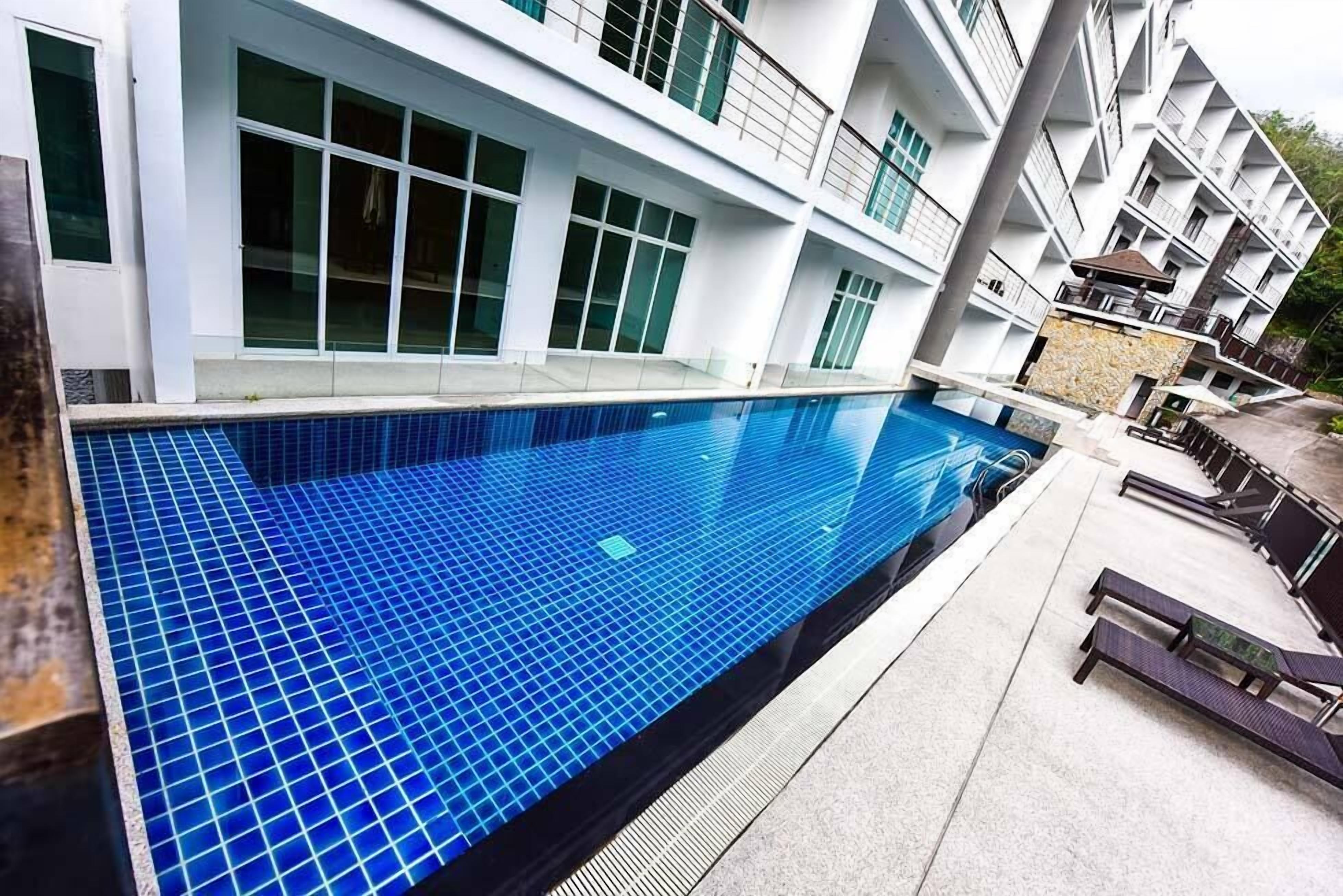 Un hotel moderno con piscina, mobiliario exterior y un edificio de varios pisos con balcones.